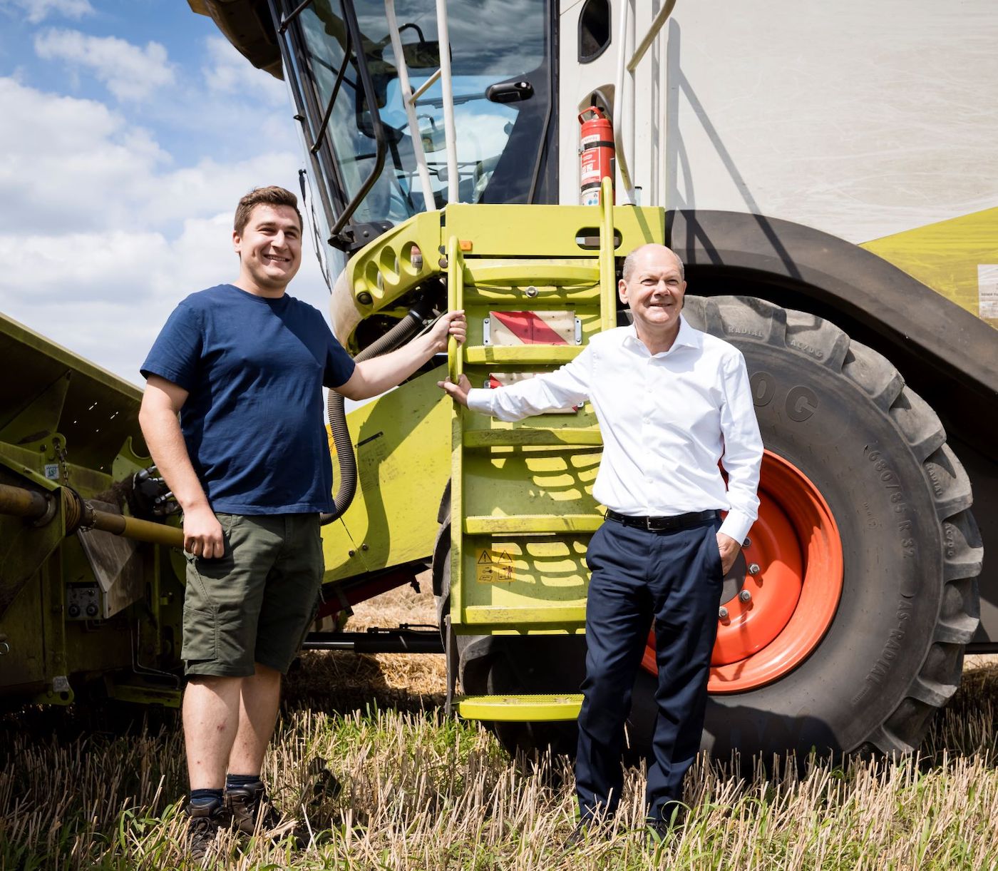 photothek Zu Besuch bei Landwirten in Potsdam-Mittelmark: Olaf Scholz und Landwirt stehen auf dem Feld vor einem Mähdrescher.